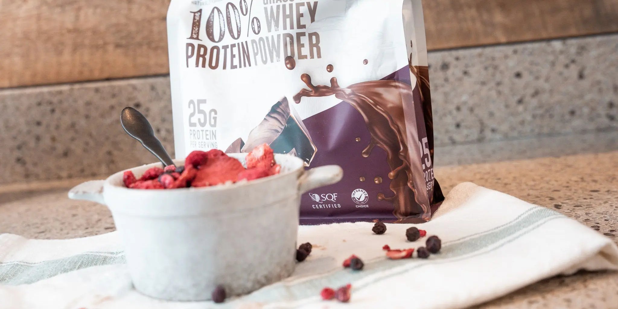 Full-sized package of Wild Society Grass-Fed Whey Protein Powder behind a bowl of protein oatmeal with dried berries on top.