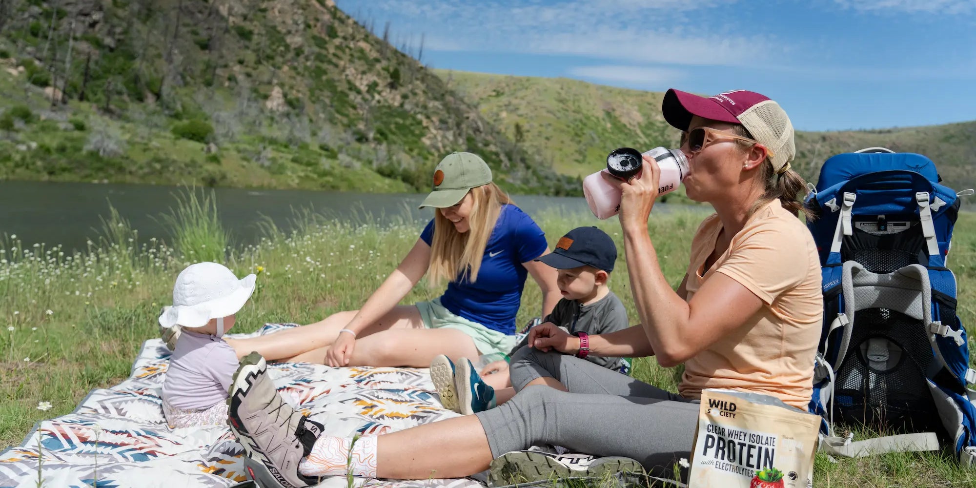 A mom in athletic gear drinking clear whey protein while on a hike with her three children.
