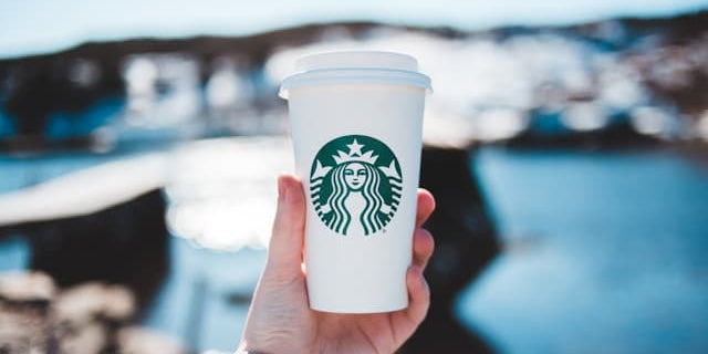 A hand holding a white paper coffee cup with a Starbucks logo containing a low carb Starbucks drink