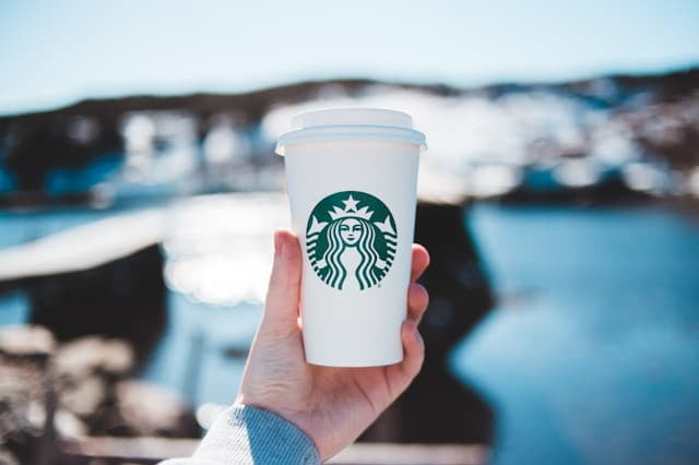 A hand holding a white paper coffee cup with a Starbucks logo containing a low carb Starbucks drink