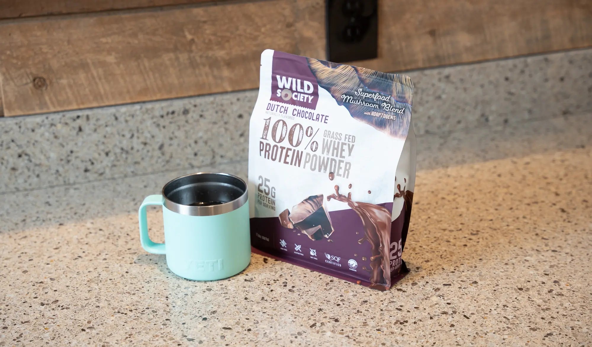 Full-size package of Wild Society Grass-Fed Whey Protein Powder next to a mug of hot coffee.