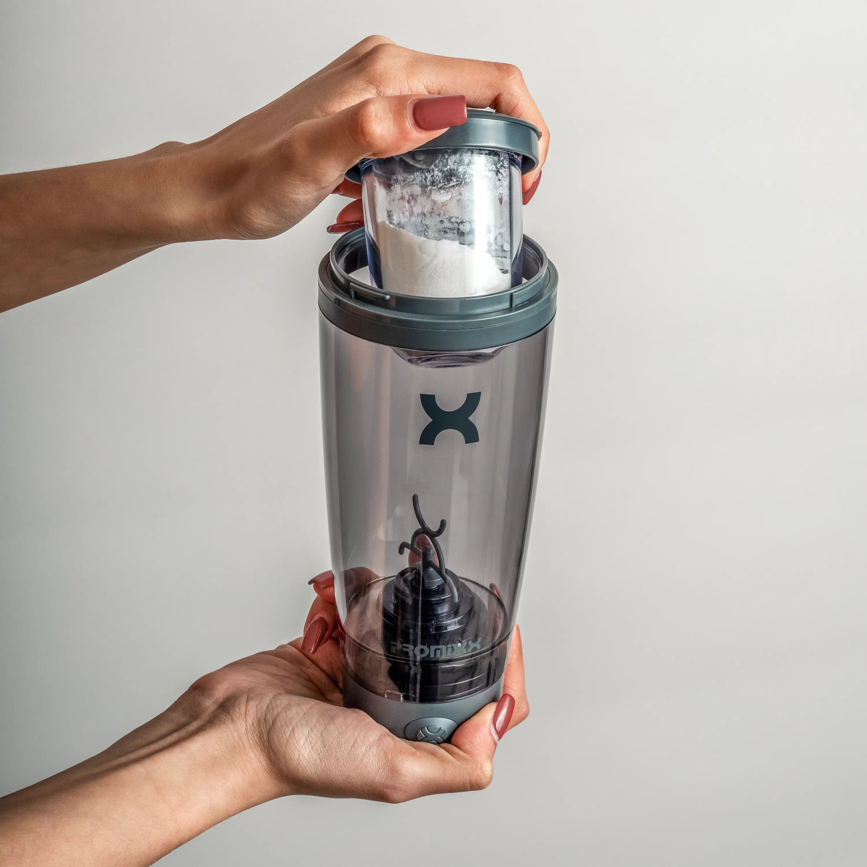 Person holding a transparent tumbler with a black lid, featuring a brand logo, against a plain background.