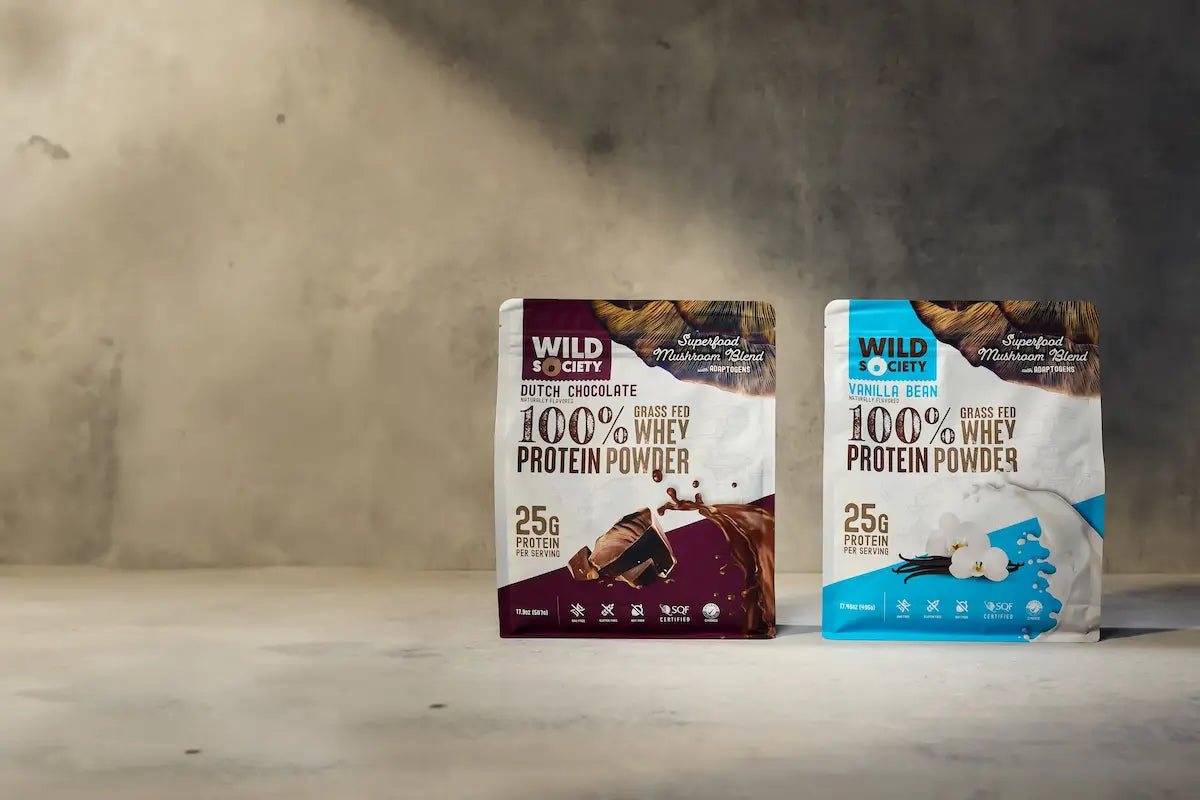 Two packages of Wild Craft 100% Whey Protein Powder on a wooden surface with a neutral background.