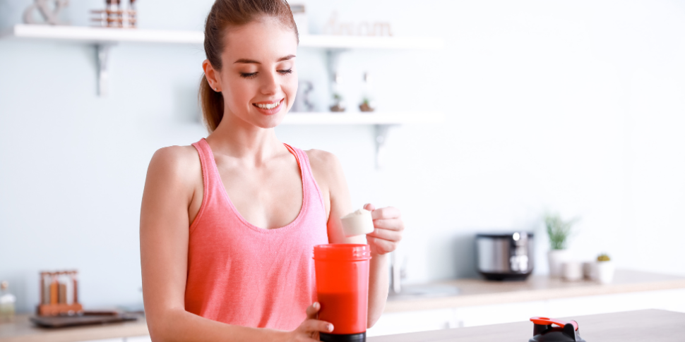 A woman in workout clothes taking a scoop of protein powder to make a morning smoothie and wonder what is the best protein powder for women?