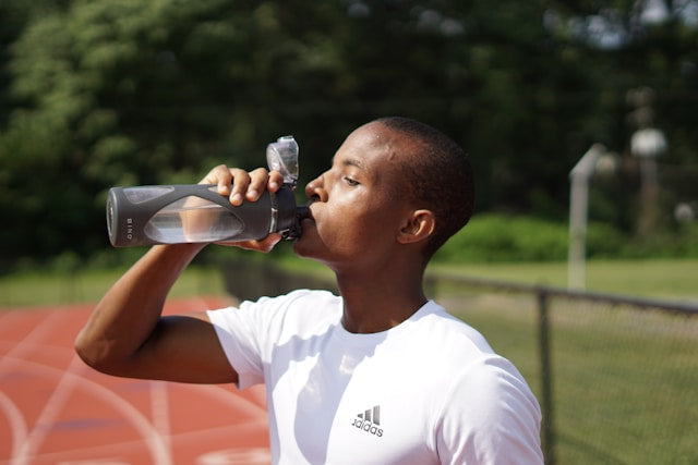 Man drinking from a shaker bottle beside a running track
