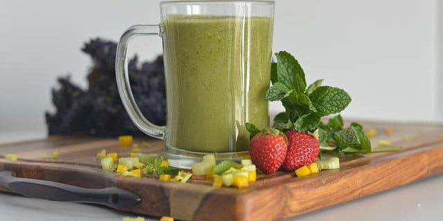 Green smoothie in a glass with strawberries and leafy greens