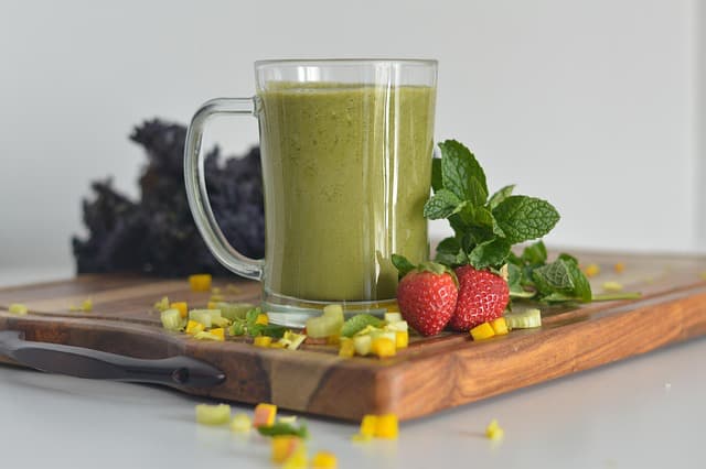 Green smoothie in a glass with strawberries and leafy greens